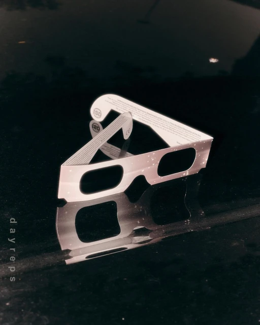 Close-up of eclipse glasses with reflective surface, featuring light and dark contrasts, with text 'dayreps' visible along the side.