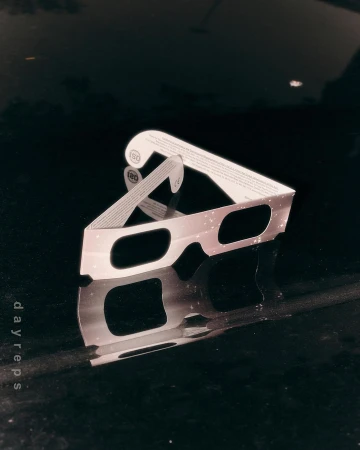Close-up of eclipse glasses with reflective surface, featuring light and dark contrasts, with text 'dayreps' visible along the side.