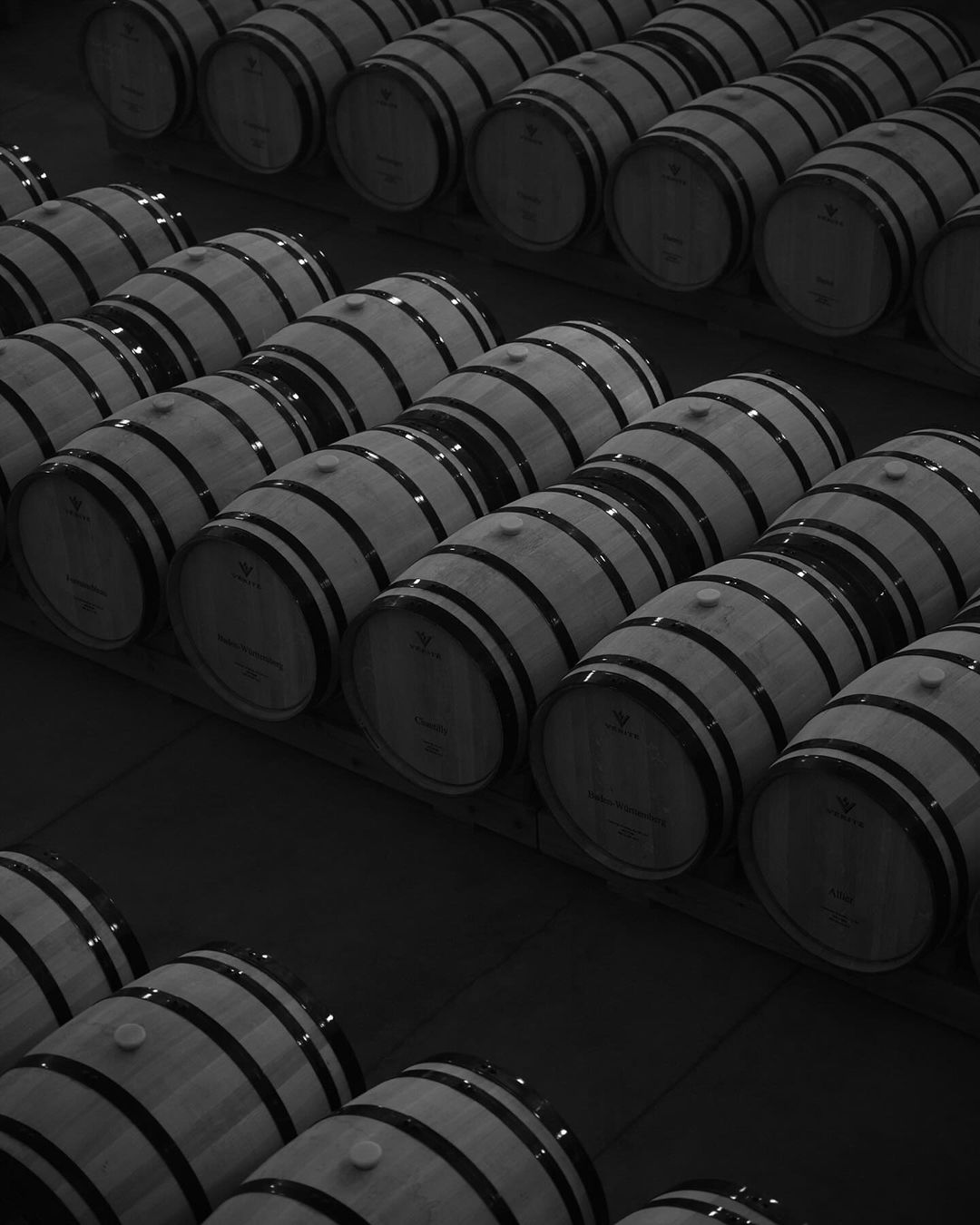 Rows of wine barrels with steel bands and bungs, tightly packed in a dark, climate-controlled environment, emphasizing wine production.