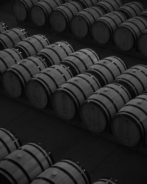 Rows of wine barrels with steel bands and bungs, tightly packed in a dark, climate-controlled environment, emphasizing wine production.
