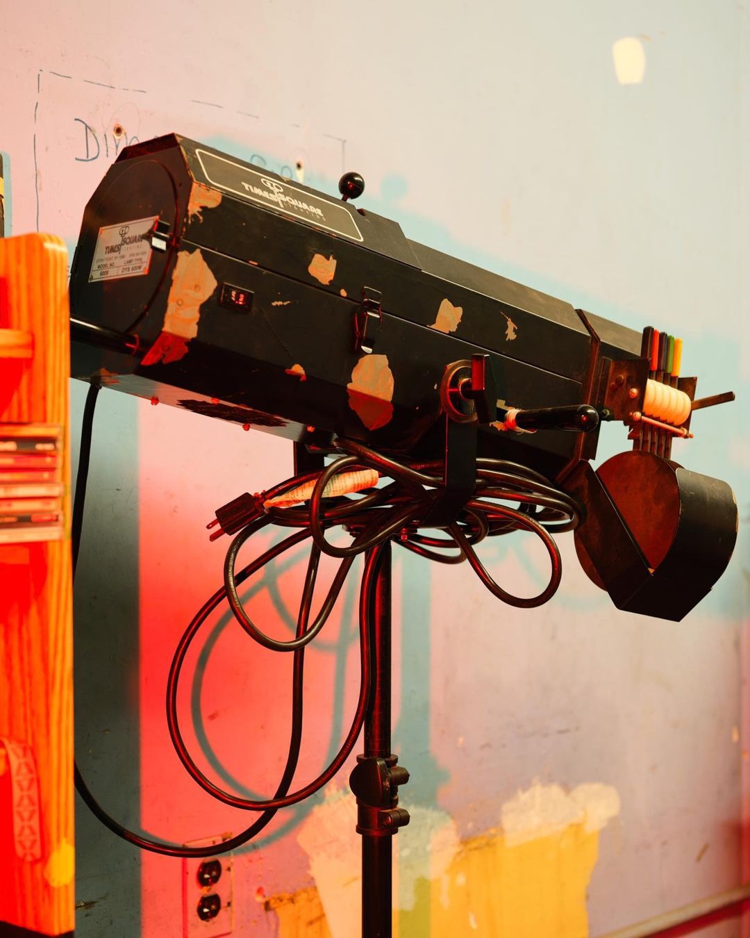 Spotlight on a stand with cords in a studio setting, featuring textures, stage lighting equipment, and a red gel, illuminated by a vivid color palette.