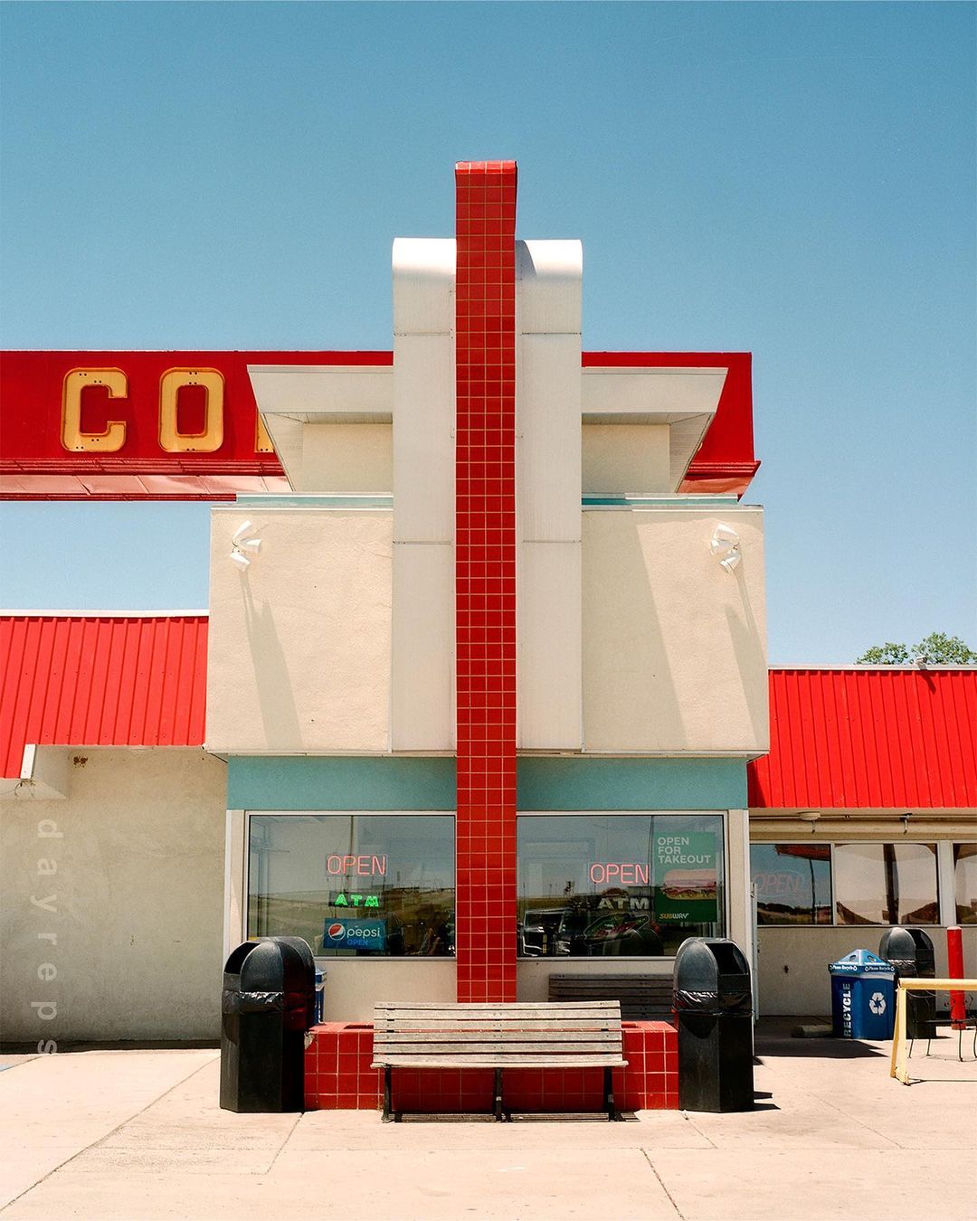 Exterior view of vintage diner with architectural details, red roof, and bench seating along the front, with clear blue sky above.