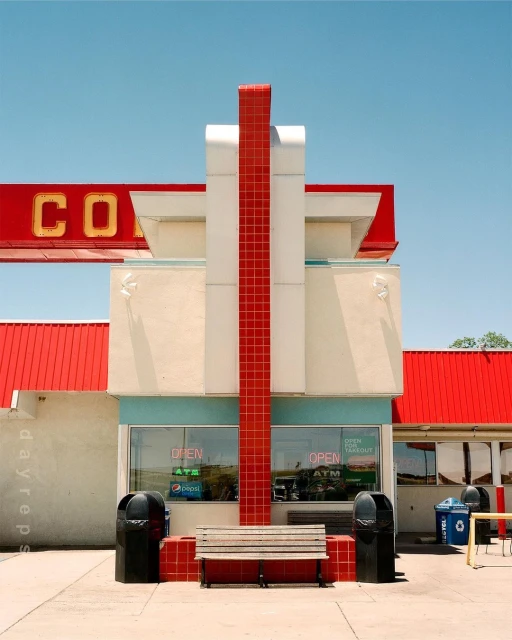 Exterior view of vintage diner with architectural details, red roof, and bench seating along the front, with clear blue sky above.