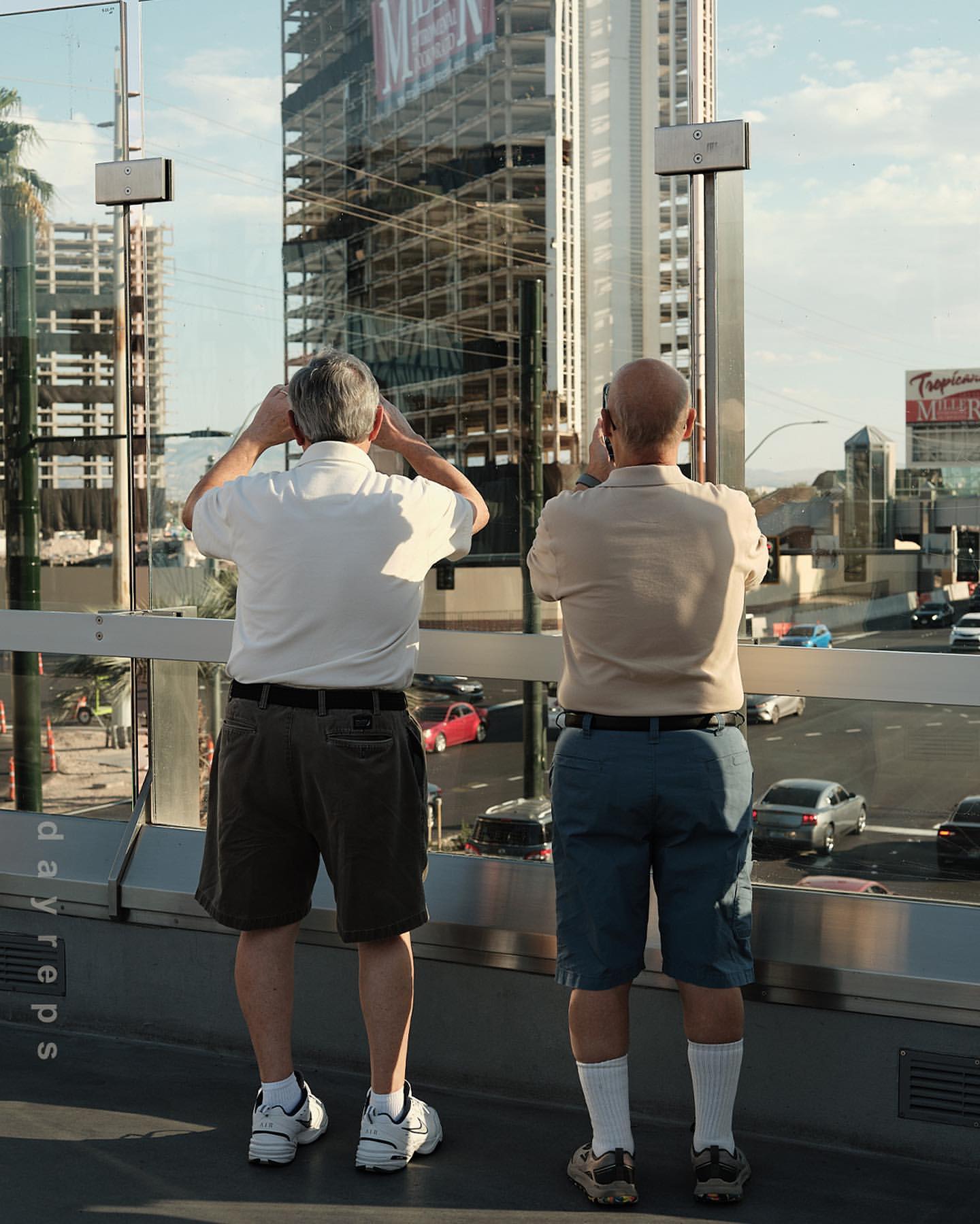 Two adult males observe a bustling city street from an elevated walkway, capturing the urban scene with a construction site background.