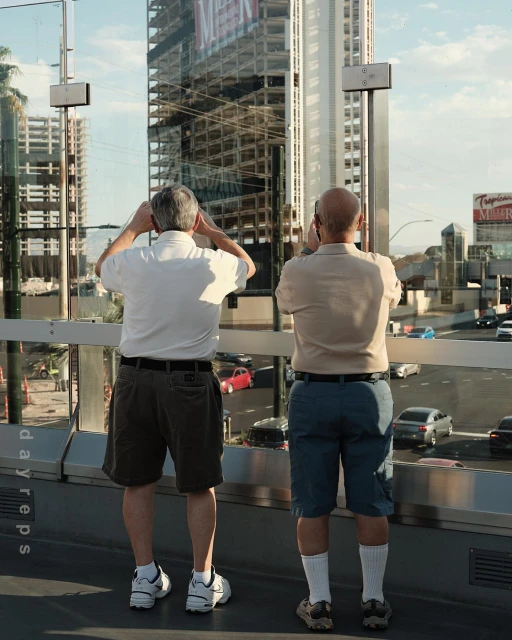 Two adult males observe a bustling city street from an elevated walkway, capturing the urban scene with a construction site background.