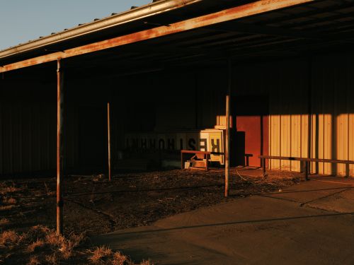 Abandoned restaurant exterior featuring an overhang, weathered facade, and muted light casting shadows on the building and surrounding area.