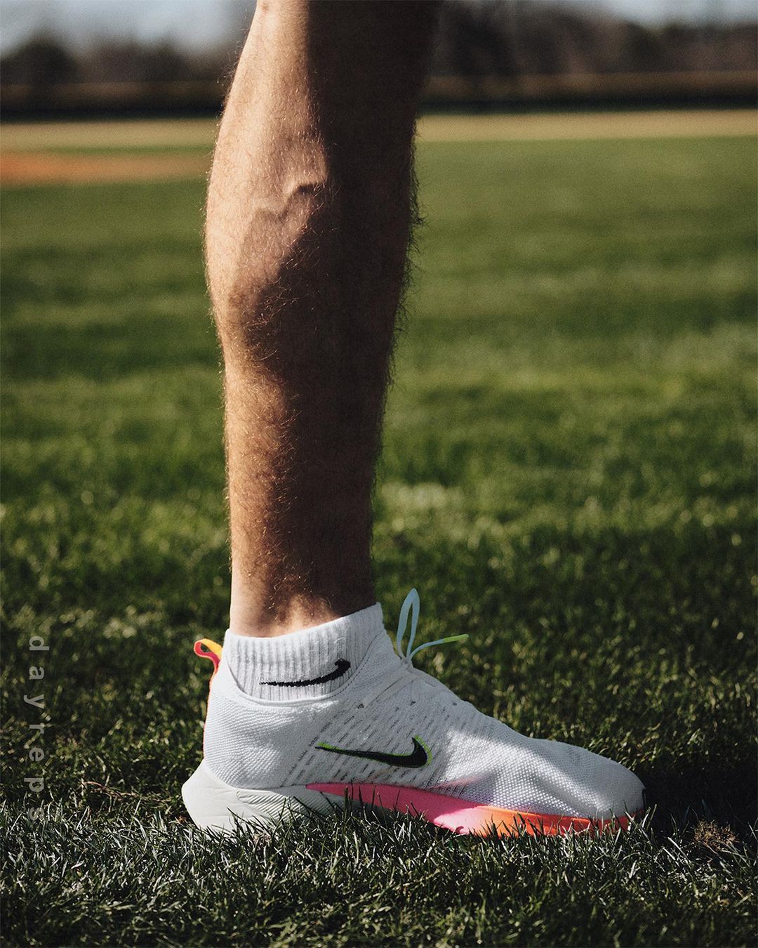Close-up of a runner's leg wearing a white Nike running shoe on a green lawn or field, captured in natural light during the day.