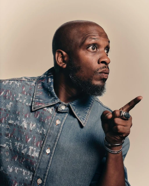 Close-up shot of a stylish bald man pointing to the side with a surprised expression wearing a unique denim button-down shirt.