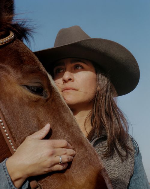 Portrait of a woman in a cowboy hat embracing a horse, set against a clear blue sky, conveying a sense of connection and outdoor lifestyle.