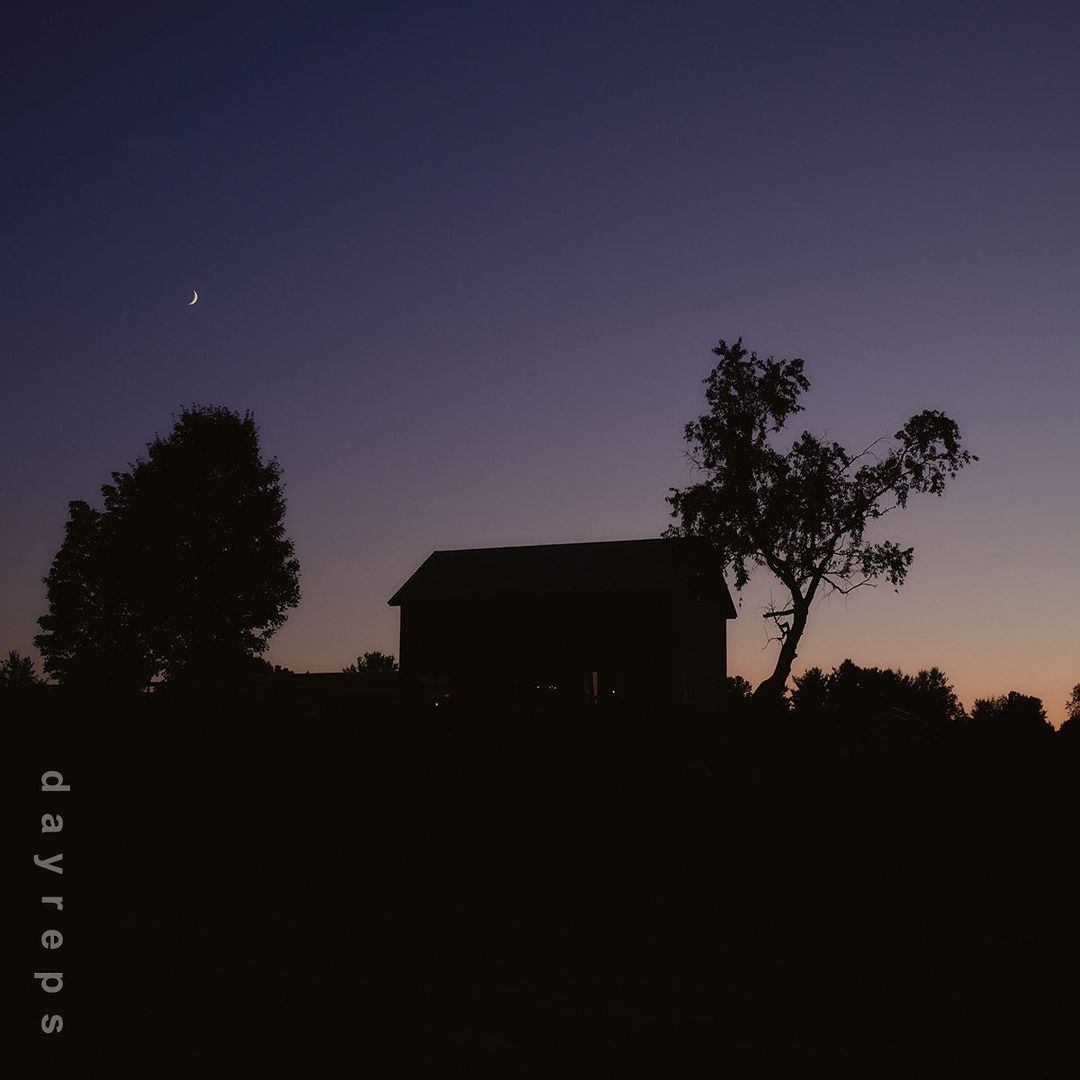 Silhouette of a barn and trees against a dusk sky with a crescent moon by Allie and Jesse