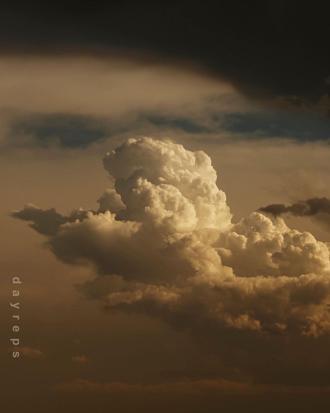 Dramatic cumulus clouds fill the frame in this low-angle shot, displaying a range of gold and gray tones against a darkened sky.