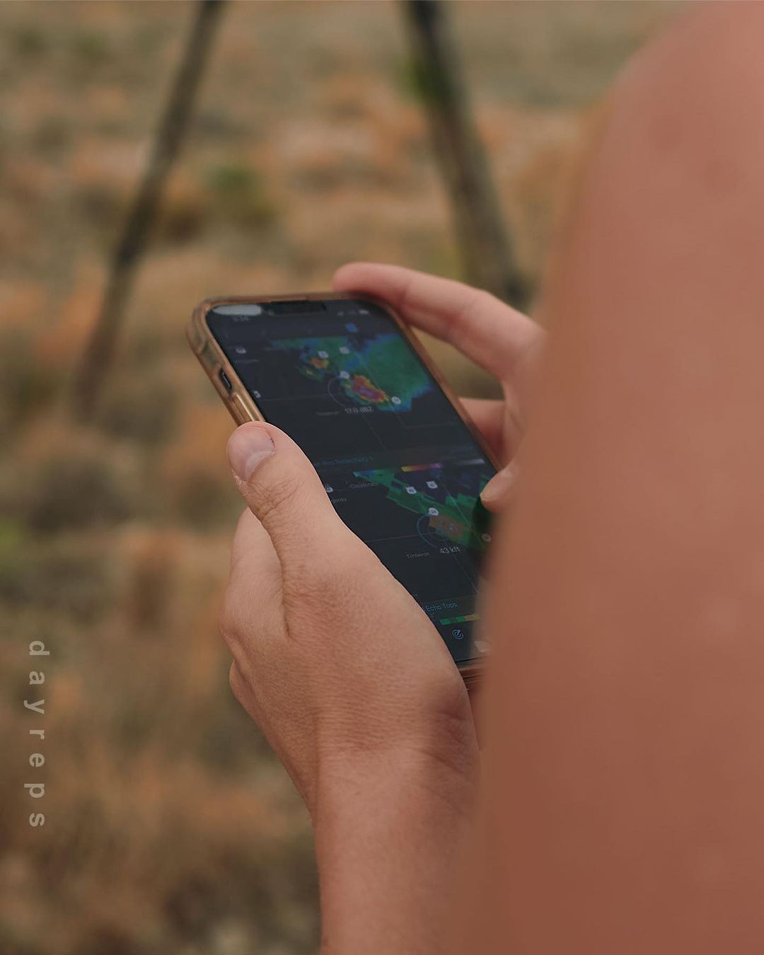 Person using a smartphone outdoors displaying a weather map. Focus on the phone screen, held by a person. Blurred background.