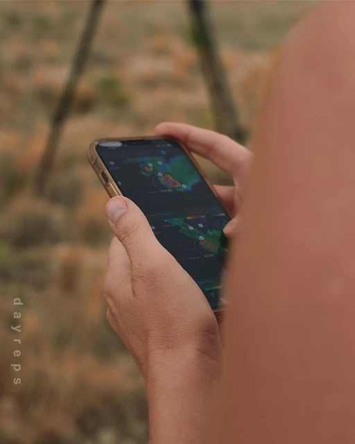 Person using a smartphone outdoors displaying a weather map. Focus on the phone screen, held by a person. Blurred background.