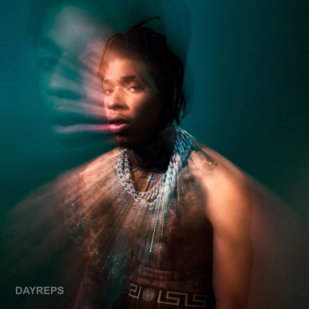 Artistic portrait of a bare-chested man with chains, a second blurred man's face, and a green and orange gradient background.