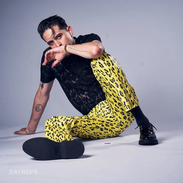 G-Eazy poses in a studio with yellow leopard-print pants and black lace top, showcasing a modern and edgy fashion style.