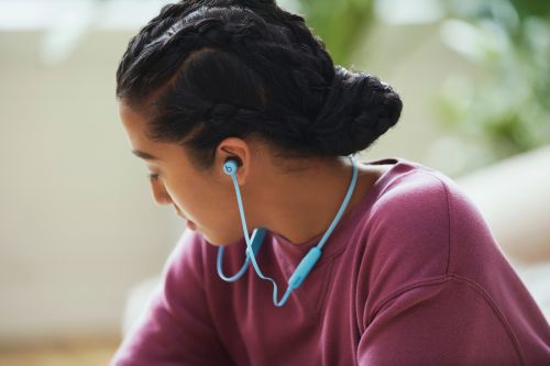 Teenage girl with braided hair wears blue wireless headphones indoors in a portrait-style, eye-level shot with natural lighting.