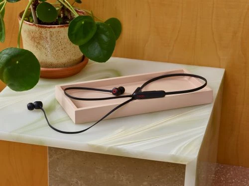 Black wireless headphones on a light pink tray sitting on a marble table with a potted plant in the background.