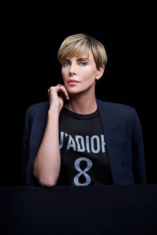 Portrait of blonde-haired woman wearing blazer over graphic t-shirt. The subject is set against a dark, neutral background in the studio.