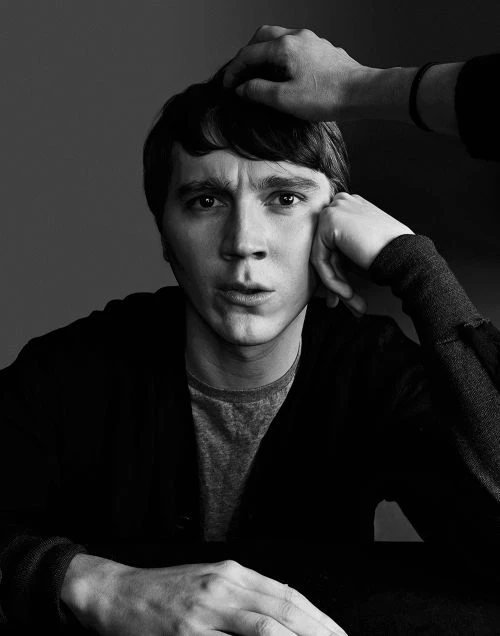 Black-and-white portrait of a man with hand touching his head, wearing a dark sweater, looking into the camera with a concerned expression.