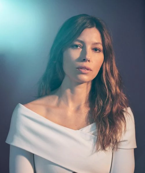 Portrait of Jessica Biel in a white dress with light shining on her face, photographed in a studio with a neutral background.