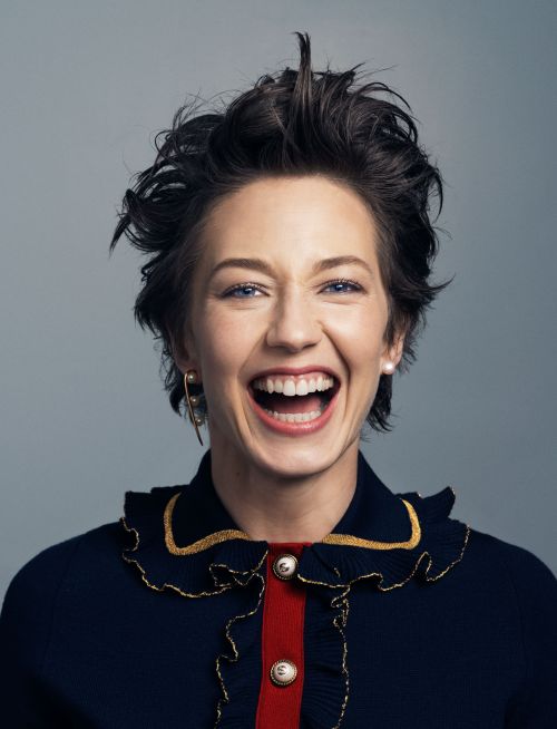 Portrait of a smiling woman with short dark hair, wearing a stylish navy blue top, set against a neutral grey background.
