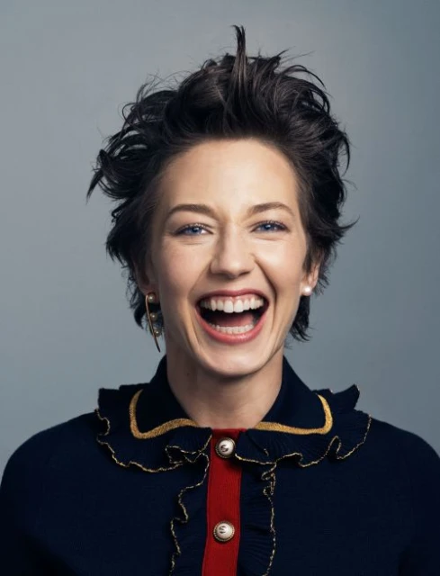 Portrait of a smiling woman with short dark hair, wearing a stylish navy blue top, set against a neutral grey background. 