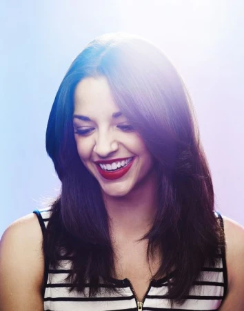 Close-up portrait of a smiling woman with dark hair and bright red lipstick wearing a striped sleeveless top against a pale background