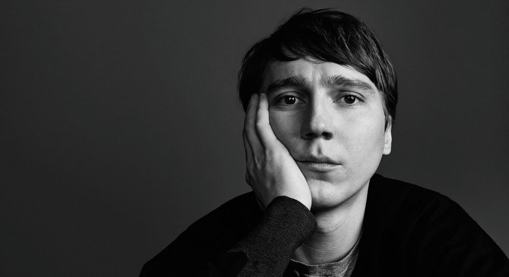 Black and white portrait of a contemplative man with hand on face, set against a dark background with soft lighting and shallow depth of field.