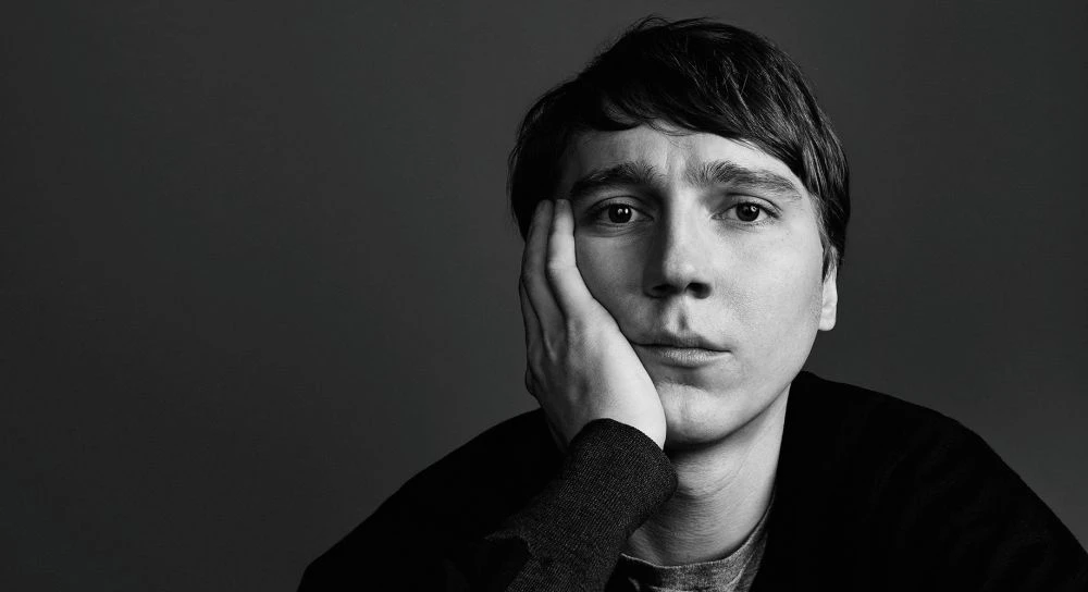 Black and white portrait of a contemplative man with hand on face, set against a dark background with soft lighting and shallow depth of field.