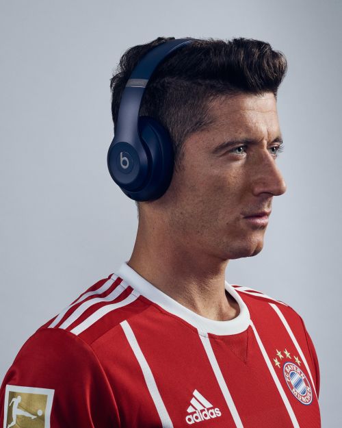 Male model in soccer jersey wears blue Beats headphones in a studio headshot against a neutral background. Close-up, clean, and modern.