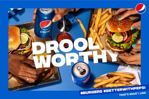 Overhead shot of Pepsi cans, burgers, and fries on a blue background, hands visible, food photography, drool-worthy concept.