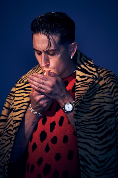 Man lighting a cigarette wearing an animal print coat and a red spotted top against a blue background