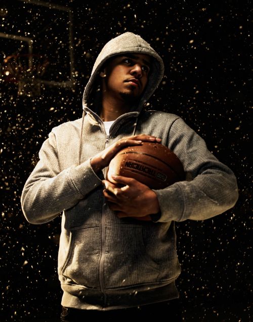 Portrait of adult male in hooded sweatshirt holding basketball in photo studio setting with black backdrop and snow effect.