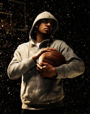 Portrait of adult male in hooded sweatshirt holding basketball in photo studio setting with black backdrop and snow effect.