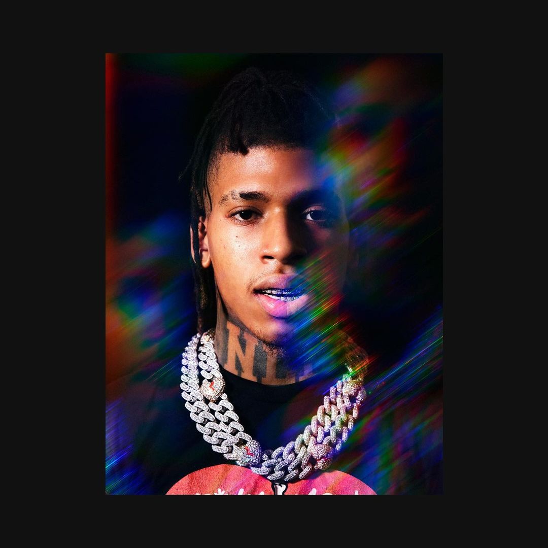 Close-up of a young adult with braided hair, wearing a diamond chain necklace, against a black background with prismatic lighting.
