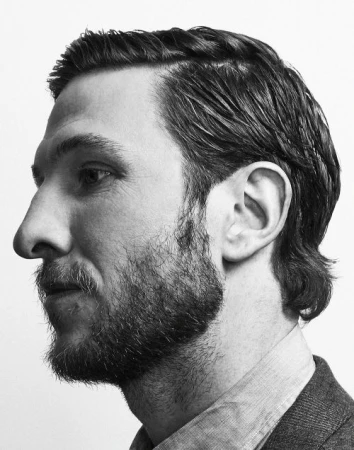 Black and white profile portrait of a bearded man in a collared shirt against a white background