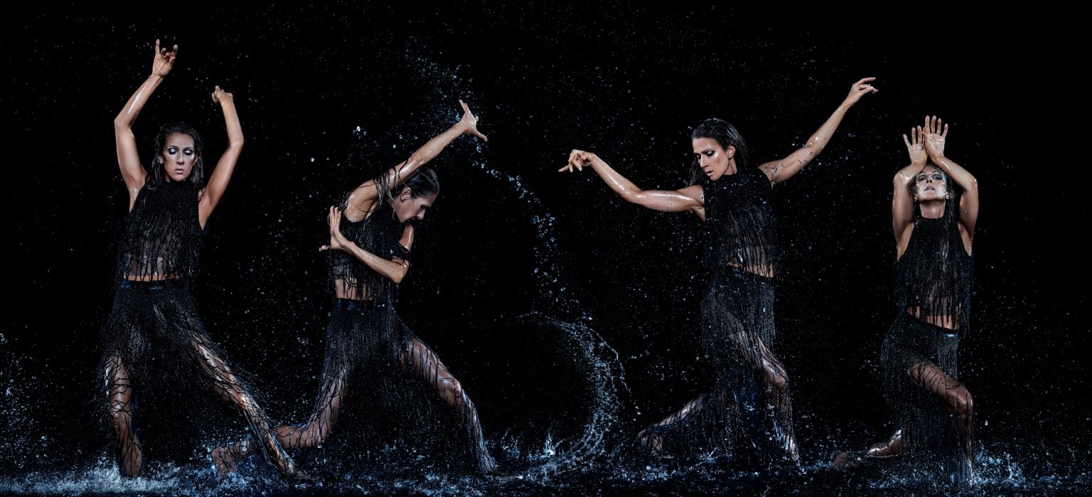 A dramatic photo features a woman in a fringed black dress, mid-dance, surrounded by splashing water against a stark black backdrop.