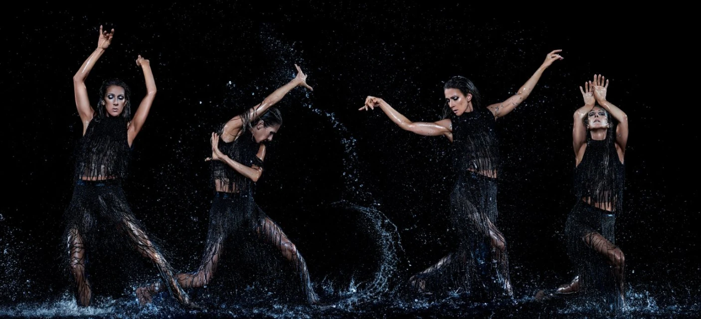 A dramatic photo features a woman in a fringed black dress, mid-dance, surrounded by splashing water against a stark black backdrop.