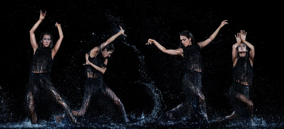 A dramatic photo features a woman in a fringed black dress, mid-dance, surrounded by splashing water against a stark black backdrop.