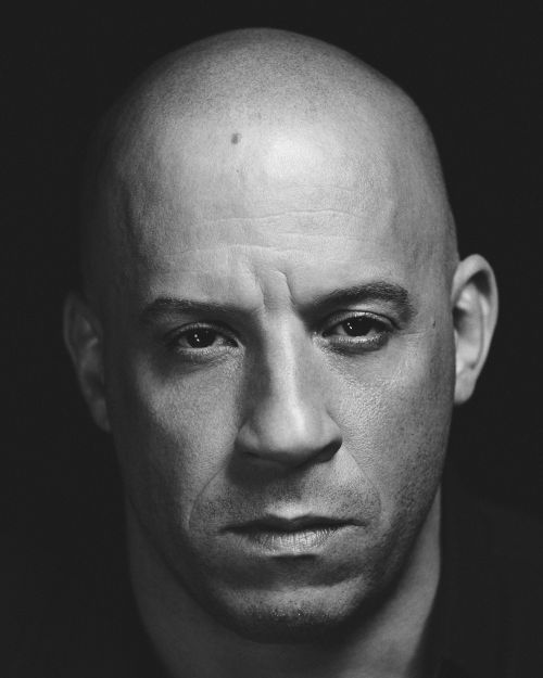 Close-up monochrome portrait of Vin Diesel against a dark background, showcasing serious expression and detailed skin texture.
