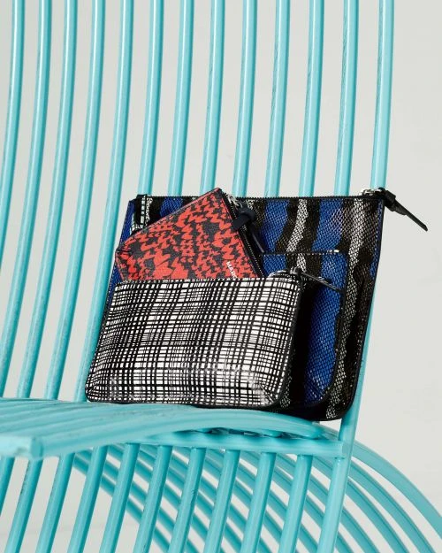 Stack of three patterned zippered pouches in red, blue, and black and white on a light blue chair in a brightly lit studio setting.