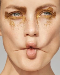 Close-up portrait of a woman with metallic gold makeup around her eyes and puckered lips.