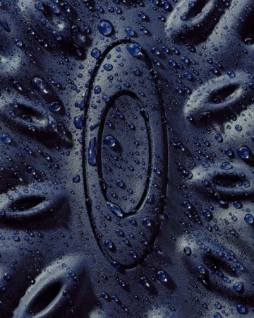 Close-up of a textured navy-blue surface with an embossed oval logo covered in water droplets, creating a wet and abstract design.