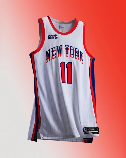 New York Knicks basketball jersey with number 11 on display against an orange and white gradient background in a studio setting.