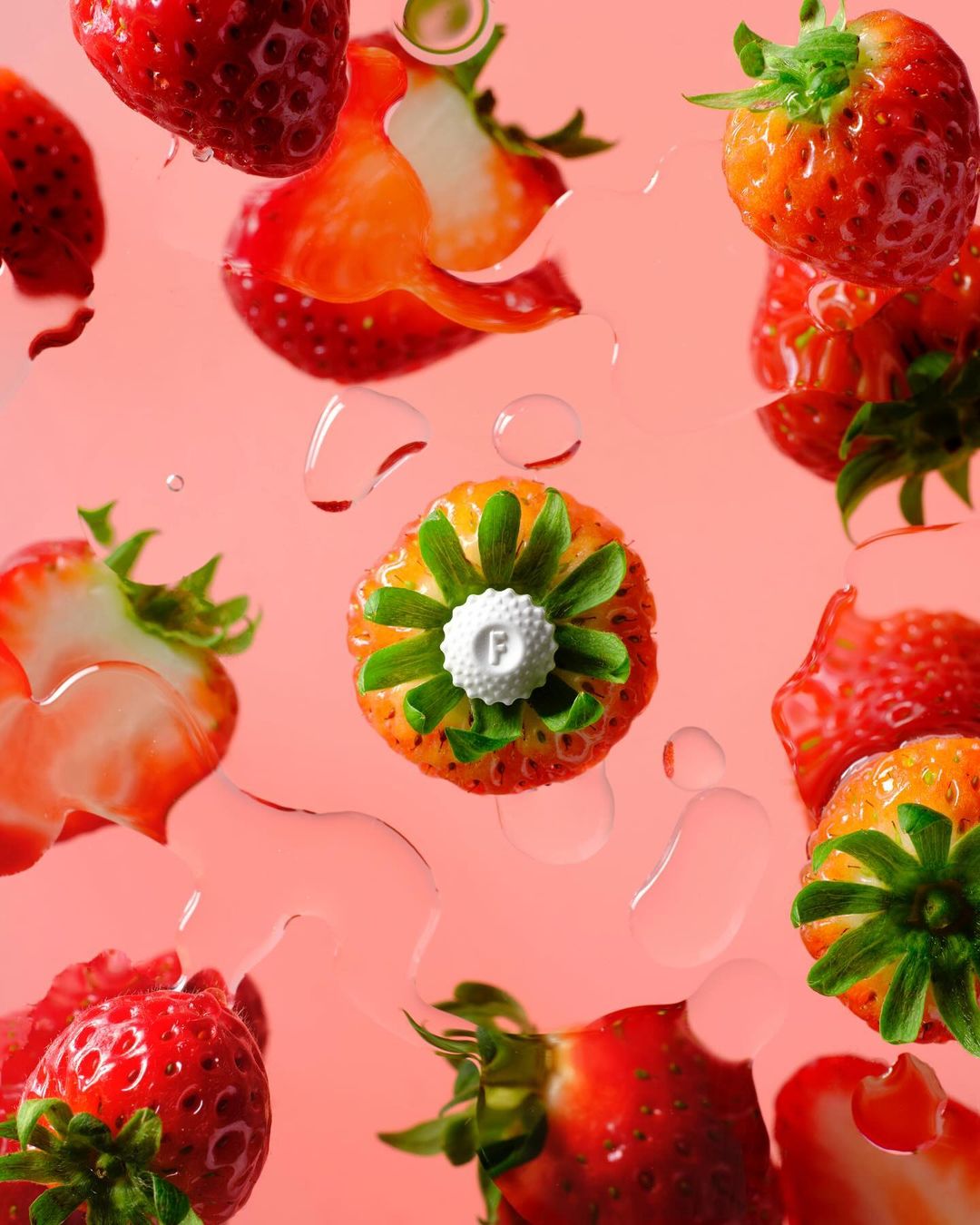 Fresh strawberries and water droplets in an overhead shot against a pink background create a bright, fruity composition.