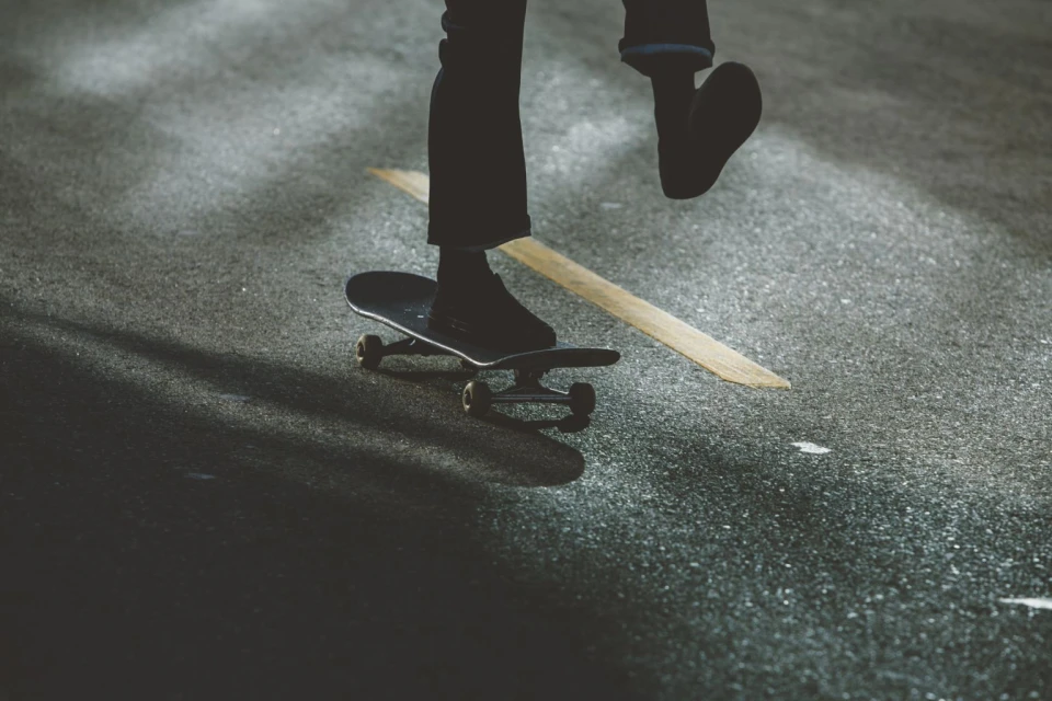 Person skateboarding on asphalt, captured from a low angle with dark color grading, focusing on movement and texture in an outdoor environment.