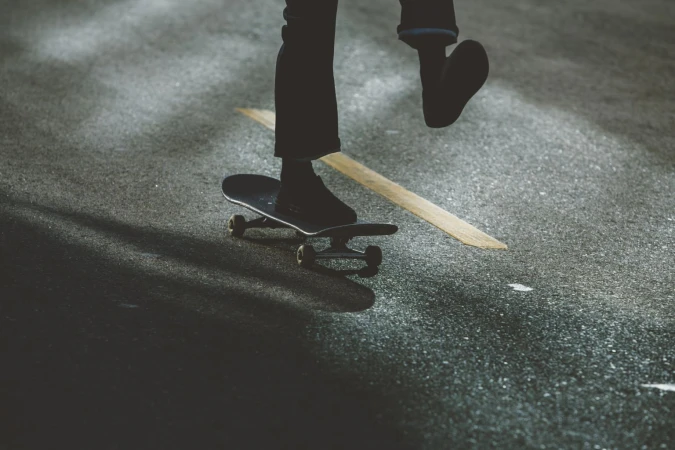 Person skateboarding on asphalt, captured from a low angle with dark color grading, focusing on movement and texture in an outdoor environment.