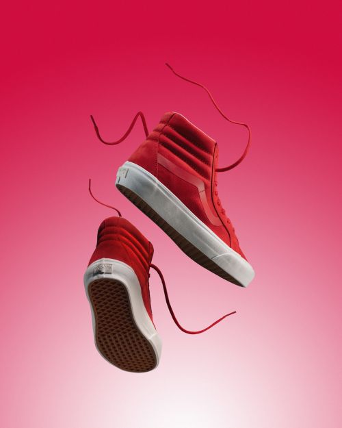Two red high-top sneakers with white soles and laces stand out against a graduated red and white background in a studio shot.