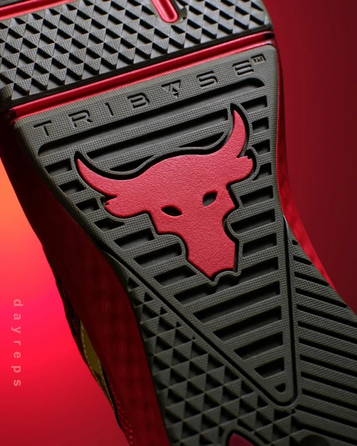 Close-up of the bottom of a red and grey athletic shoe with a red bull logo and embossed 'TRIBASE' text on a red gradient background.