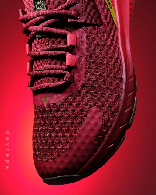 Close-up studio shot of a red athletic shoe featuring a woven texture, visible laces, and a red and yellow brand logo.